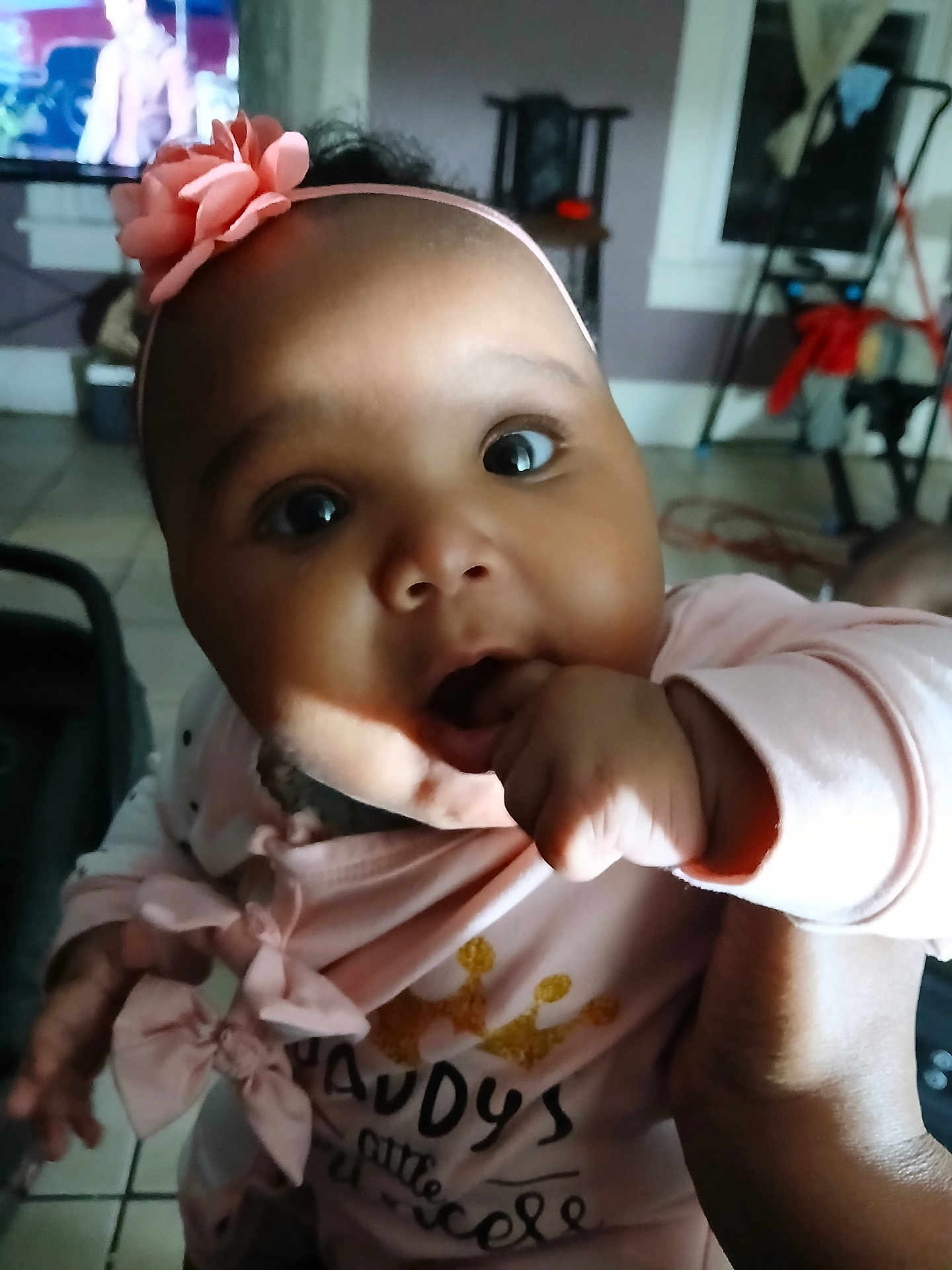 Modestie joined the competition — help win amazing prizes! baby, infant, pink_headband, flower, hand, fingers, face, eyes, clothing, indoor, floor_tile, television, furniture, person, cute, portrait, child, sitting, home, family