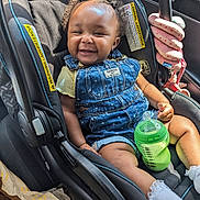 Hazel is registered to the contest to win money with this photo: baby, car_seat, denim_overall, smiling, child, sippy_cup, toy, pink, yellow_shirt, curly_hair, indoor, seatbelt, car_interior, happy, cute, infant, portrait, clothing, hands, feet