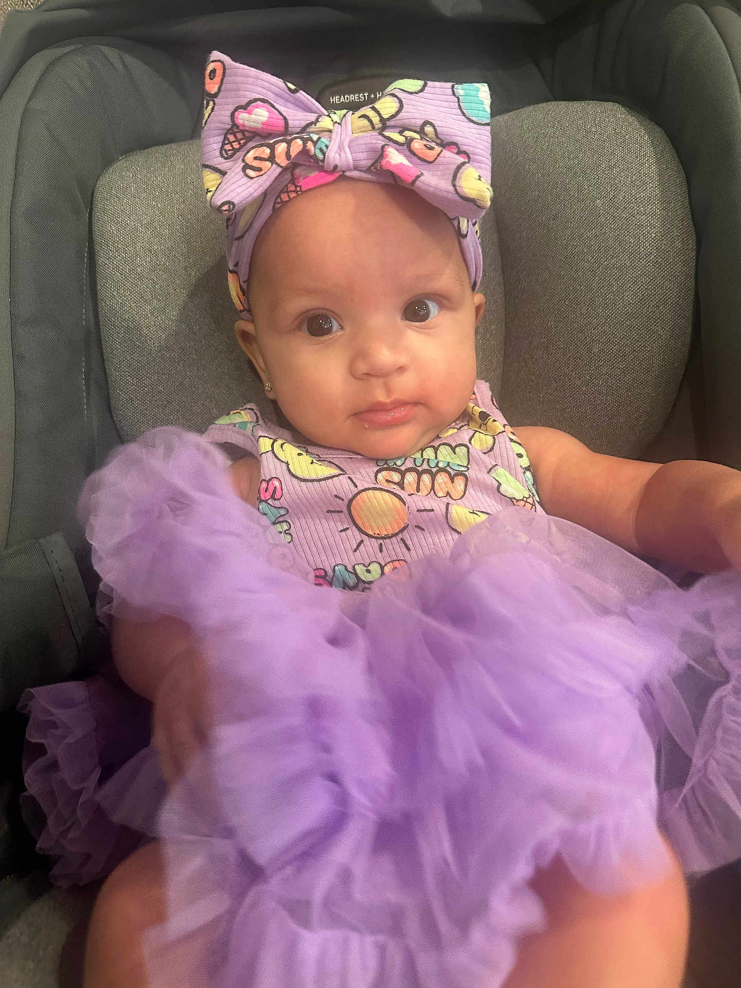 Layla Rose is registered to the contest to win money with this photo: baby, child, car_seat, purple, headband, dress, tulle, infant, cute, portrait, smiling, person, clothing, accessory, seat, indoor, young_child, happy, headwear, fashion