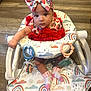 baby, child, infant, bow, headband, red_dress, baby_walker, rainbow_pattern, socks, flooring, wood_floor, toy_rings, curious_expression, indoor, cute, seated, colorful, adorable, person, young_child