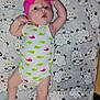 baby, infant, child, onesie, pink_bow, headband, blanket, sheep_pattern, lying_down, cute, arms_up, curious, indoors, soft_texture, sleepwear, white_clothing, green_whales, pink_whales, portrait, human