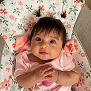 Genesis Andrea Muñoz is registered to the contest to win money with this photo: baby, infant, child, pigtails, hair_bows, pink_clothing, floral_pattern, cushion, seated, indoor, cute, small_hands, portrait, looking_up, soft_lighting, adorable, chubby_cheeks, happy, home, comfort