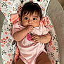 baby, infant, child, pigtails, bows, pink_onesie, floral_pattern, baby_seat, cute, hand_in_mouth, wide_eyes, indoors, soft_lighting, portrait, young_child, adorable, sitting, person, skin, expression