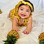 Zoe joined the competition — help win amazing prizes! baby, child, smiling, yellow_clothing, headband, pineapple, fruit, crawling, happy, blue_eyes, indoor, white_background, cute, infant, playful, portrait, hands, face, expression, closeup