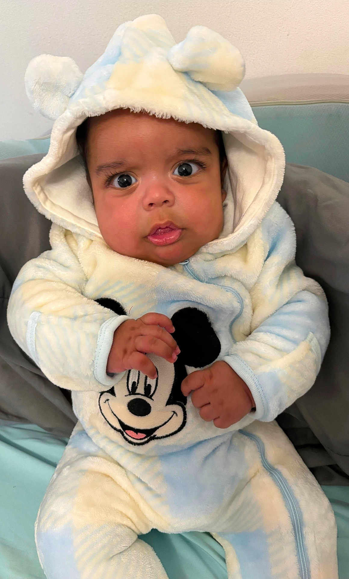 Christopher is registered to the contest to win money with this photo: baby, infant, child, hooded_outfit, mickey_mouse, onesie, blue, white, big_eyes, hands, close_up, portrait, surprised_expression, plush, seat, blanket, indoor, cozy, eyelashes, pajamas