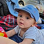 baby, child, blue_cap, blanket, colorful, curious, outdoor, car, face, wide_eyes, reaching, lying_down, plaid_blanket, soft_blanket, person, infant, close_up, casual, daytime, cute