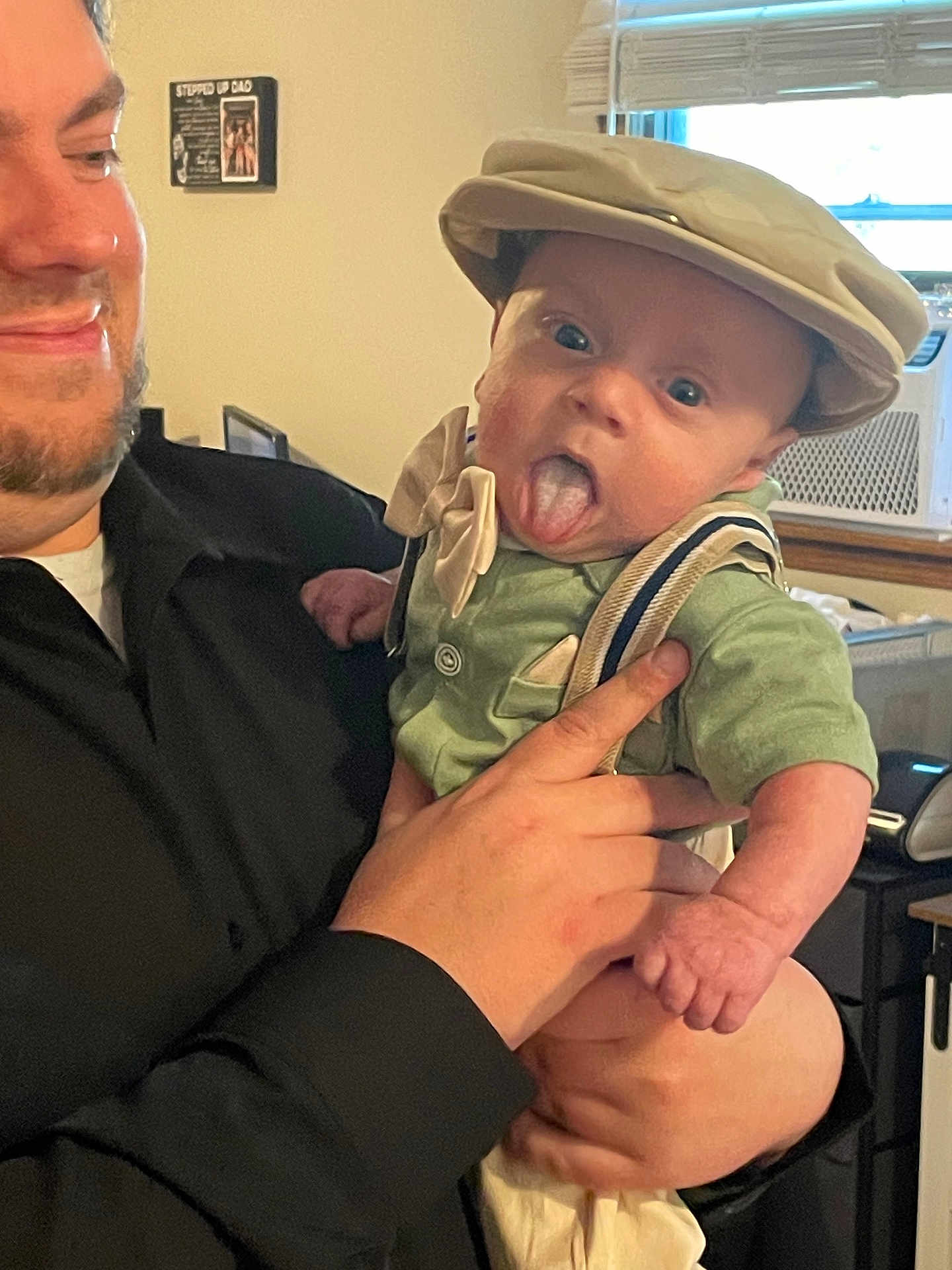 Maverick joined the competition — help win amazing prizes! baby, child, adult, person, face, tongue, hat, clothing, suspenders, hand, smile, indoor, window, air_conditioner, furniture, portrait, cute, expression, holding, funny