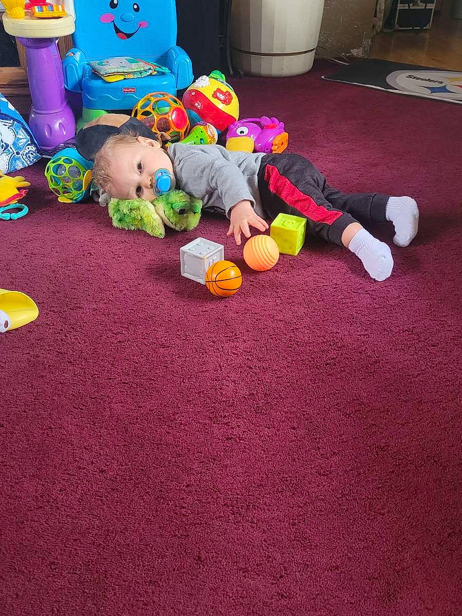 Storm is registered to the contest to win money with this photo: baby, baby_products, baby_toys, carpet, child, floor, flooring, fun, games, grass, houseplant, human_leg, leisure, person, play, purple, room, stuffed_toy, toddler, toy