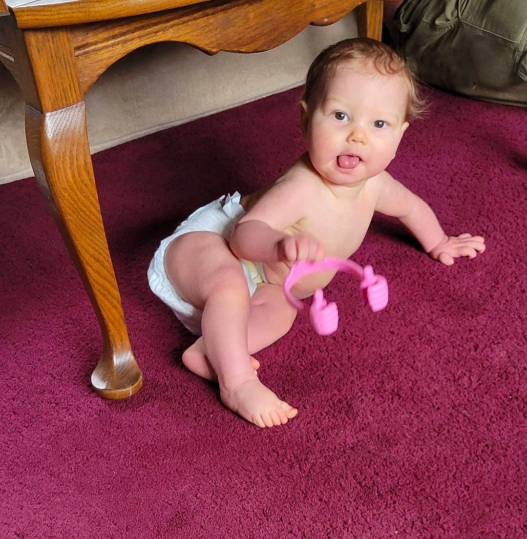 Storm is registered to the contest to win money with this photo: baby, baby_toddler_clothing, chair, cheek, comfort, floor, flooring, foot, human_body, human_leg, iris, lap, person, sitting, smile, sock, table, thigh, thumb, toddler