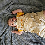Matteo is registered to the contest to win money with this photo: baby, infant, pacifier, blanket, clothing, yellow, winnie_the_pooh, cute, soft_texture, lying_down, child, face, portrait, indoors, comfort, sleepwear, happy, skin, small_hands, baby_outfit