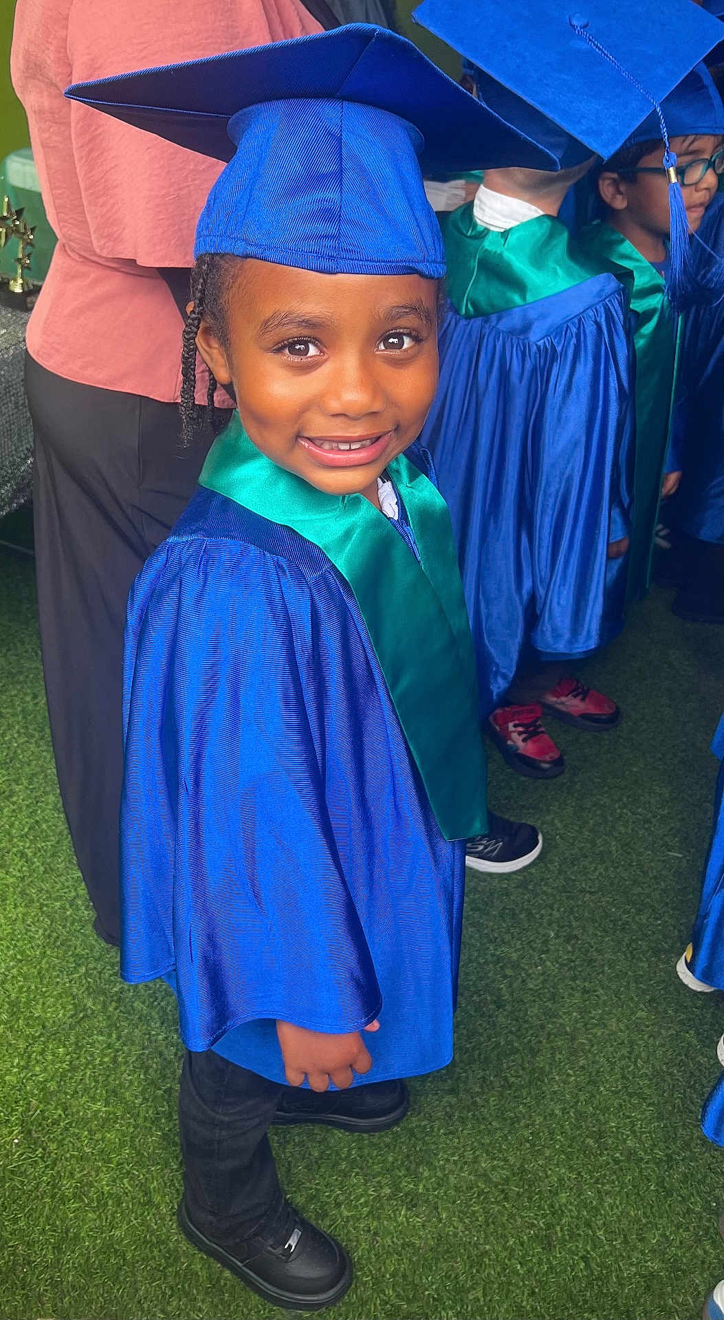 Carson joined the competition — help win amazing prizes! child, graduation, blue_gown, graduation_cap, smiling, green_stole, indoor, group, people, black_shoes, braided_hair, happy, celebration, portrait, event, young_student, education, ceremony, person, crowd