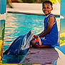 child, boy, dolphin, pool, water, dock, smile, blue_clothing, outdoor, summer, animal, pet, marine_life, nature, playful, vacation, happy, portrait, tropical, cartoon_border