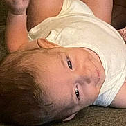 Yahya is registered to the contest to win money with this photo: baby, infant, child, white_clothing, sleeveless_shirt, lying_down, curious_expression, raised_arm, skin, head, face, eyes, smile, hair, person, indoors, couch, fabric, texture, relaxed