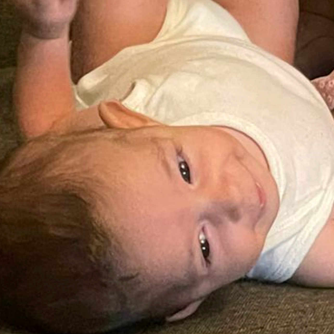 Yahya is registered to the contest to win money with this photo: baby, child, couch, curious_expression, eyes, fabric, face, hair, head, indoors, infant, lying_down, person, raised_arm, relaxed, skin, sleeveless_shirt, smile, texture, white_clothing