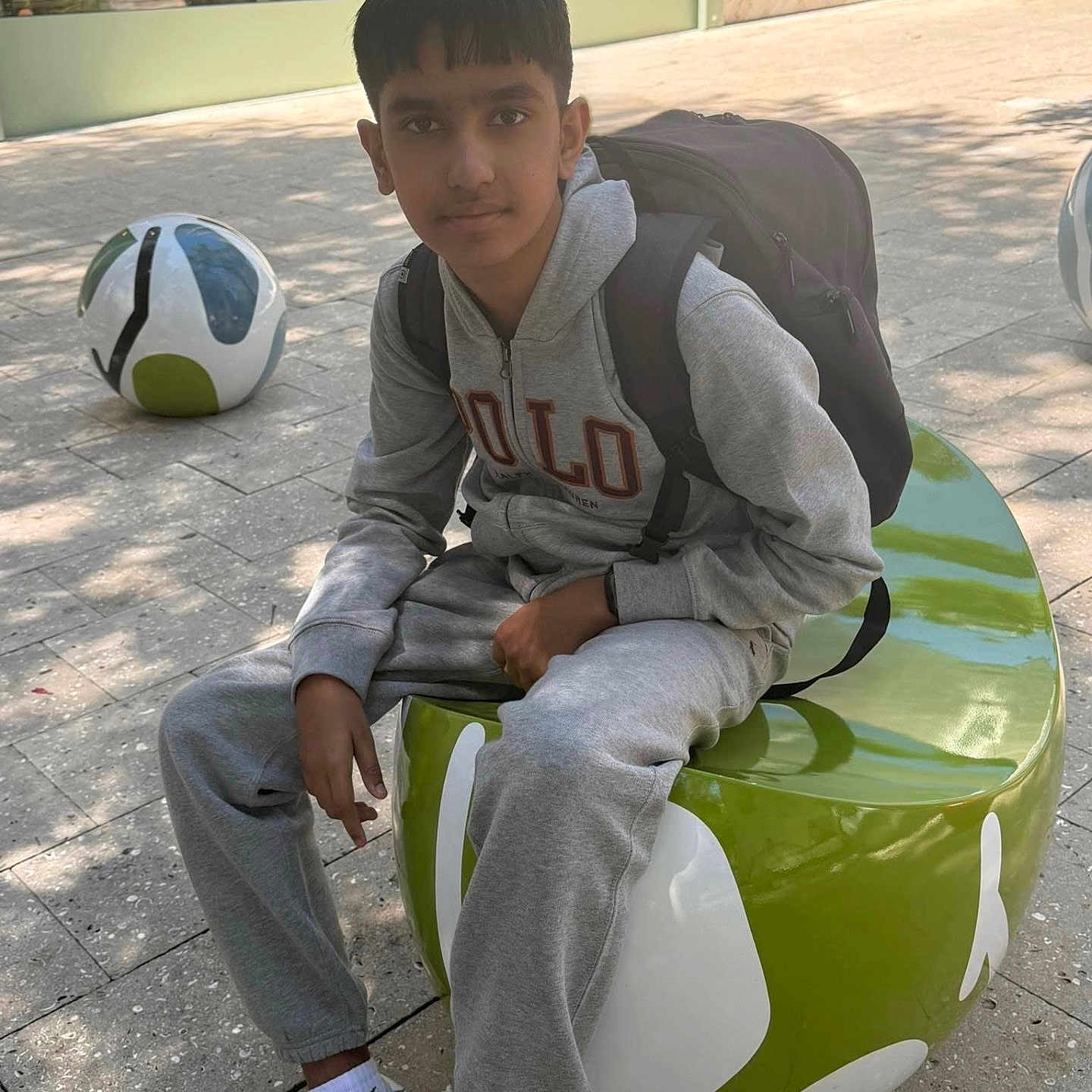 Vippin Singh joined the competition — help win amazing prizes! backpack, calm_expression, casual_pose, daylight, decorative_spheres, green_seat, grey_tracksuit, modern_building, outdoor_seating, paved_ground, portrait, relaxed, shadows, short_hair, sportswear, street_furniture, teenage_boy, urban_environment, white_sneakers, young_person