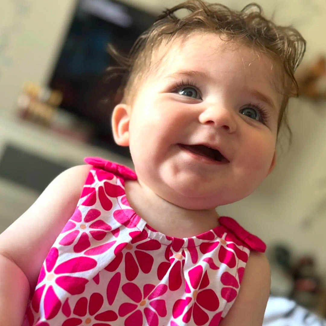 Ambre participe au concours pour gagner de l'argent avec cette photo : baby, blue_eyes, child, closeup, curly_hair, cute, domestic, dress, face, floral_pattern, happy, indoor, infant, person, pink, portrait, skin, smiling, white, young