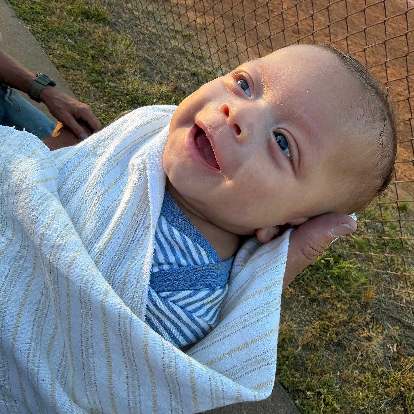 Xielynn joined the competition — help win amazing prizes! baby, child, smiling, blanket, striped_clothing, hand, outdoor, fence, grass, sunset, person, portrait, happy, head, face, holding, infant, closeup, wrapped, casual