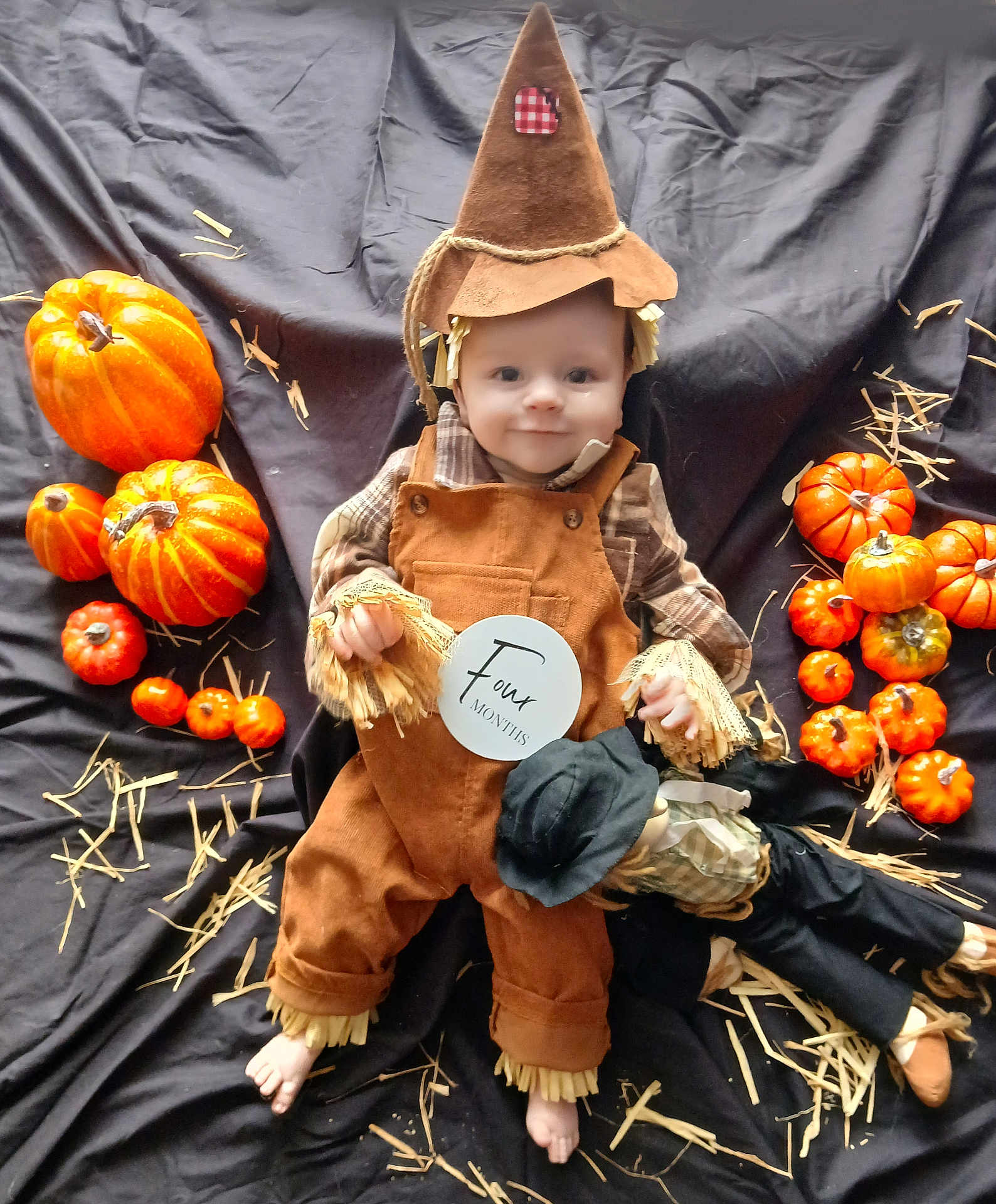 Albie is registered to the contest to win money with this photo: baby, scarecrow_costume, pumpkins, orange, black_cloth, straw, doll, infant, hat, cute, autumn, fall, holiday, smiling, costume, child, seasonal, celebration, portrait, four_months