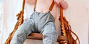 Albie is registered to the contest to win money with this photo: baby, child, swing, wooden_swing, ropes, checkered_pants, suspenders, cap, bare_chest, feet, hands, white_background, indoor, infant, cute, portrait, clothing, person, fashion, relaxing