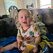 Joseph is registered to the contest to win money with this photo: toddler, child, smiling, indoors, couch, blanket, snack, living_room, window, fan, kitchen, appliance, clothing, sitting, happy, person, face, home, casual, relaxed