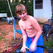 Michael joined the competition — help win amazing prizes! child, boy, shirtless, blue_shorts, bicycle, outdoor, exercise_equipment, building, window, grass, dirt, tree, motion_blur, summer, casual, young, active, play, person, nature