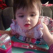 Raven is registered to the contest to win money with this photo: baby, child, toy, playset, colorful, ruffled_clothing, indoor, couch, curious, infant, face, person, closeup, soft_focus, expression, young_child, seated, activity, playtime, home