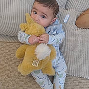 Karm joined the competition — help win amazing prizes! baby, child, stuffed_animal, plush_toy, couch, pajamas, indoor, cute, soft_toy, infant, seated, cozy, childhood, looking_up, home, comfort, fabric, cushion, toy, relaxation