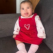 Harmony is registered to the contest to win money with this photo: baby, child, infant, smiling, happy, portrait, seated, sofa, couch, red_dress, pink_shirt, pink_socks, clothing, heart, indoors, home, furniture, photography, face, family_photo