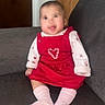 baby, child, infant, smiling, happy, portrait, seated, sofa, couch, red_dress, pink_shirt, pink_socks, clothing, heart, indoors, home, furniture, photography, face, family_photo