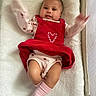 baby, infant, child, portrait, lying_down, crib, blanket, red_outfit, heart, pink_socks, smiling, wide_eyed, arms_raised, indoor, nursery, cozy, textile, bedding, crib_mesh, photography