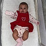 Harmony is registered to the contest to win money with this photo: baby, infant, child, portrait, lying_down, bassinet, crib, blanket, white_blanket, red_outfit, pink_clothing, pinafore, socks, heart_design, wide_eyed, looking_at_camera, indoor, nursery, cozy, photography