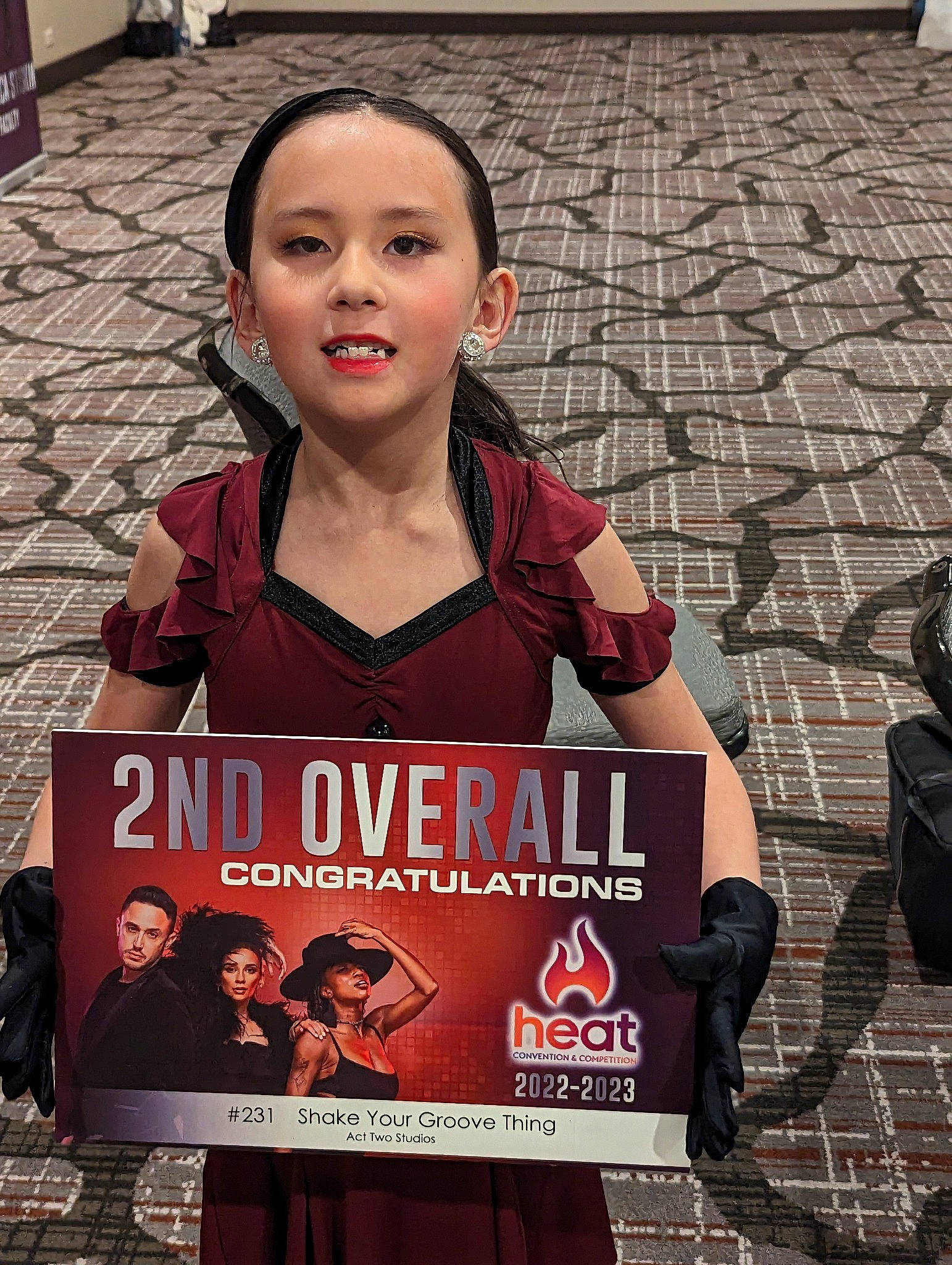 Olivia is registered to the contest to win money with this photo: advertising, brick, child, event, eyewear, face, fashion, flooring, font, logo, pattern, pedestrian, person, photo_caption, recreation, sitting, street, t_shirt