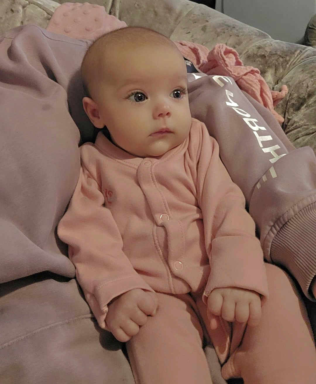 Lilah is registered to the contest to win money with this photo: baby, blanket, calm, child, couch, cozy, cute, expression, face, hands, indoor, infant, person, pink_pajamas, plush, portrait, relaxed, seated, soft_lighting, young