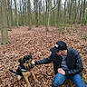 Aïko a rejoint le concours — aidez-le/la à gagner de superbes lots ! animal, autumn, black_cap, brown_leaves, canine, casual_clothing, crouching, dog, forest, friendship, happy_dog, leather_jacket, leaves, man, nature, outdoor, person, petting, playful, trees