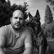 Shelby participe au concours pour gagner de l'argent avec cette photo : animal, beard, black_and_white, canine, casual_clothing, companion, dog, german_shepherd, grass, man, mature, nature, outdoor, person, pet, portrait, serious, short_sleeve_shirt, tree, watchful