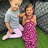 children, girls, smiling, happy, outdoor, playground, portrait, friends, sisters, posing, toddler, dress, floral_dress, pink_pants, gray_shirt, curly_hair, braided_hair, chain_link_fence, artificial_grass, play_area