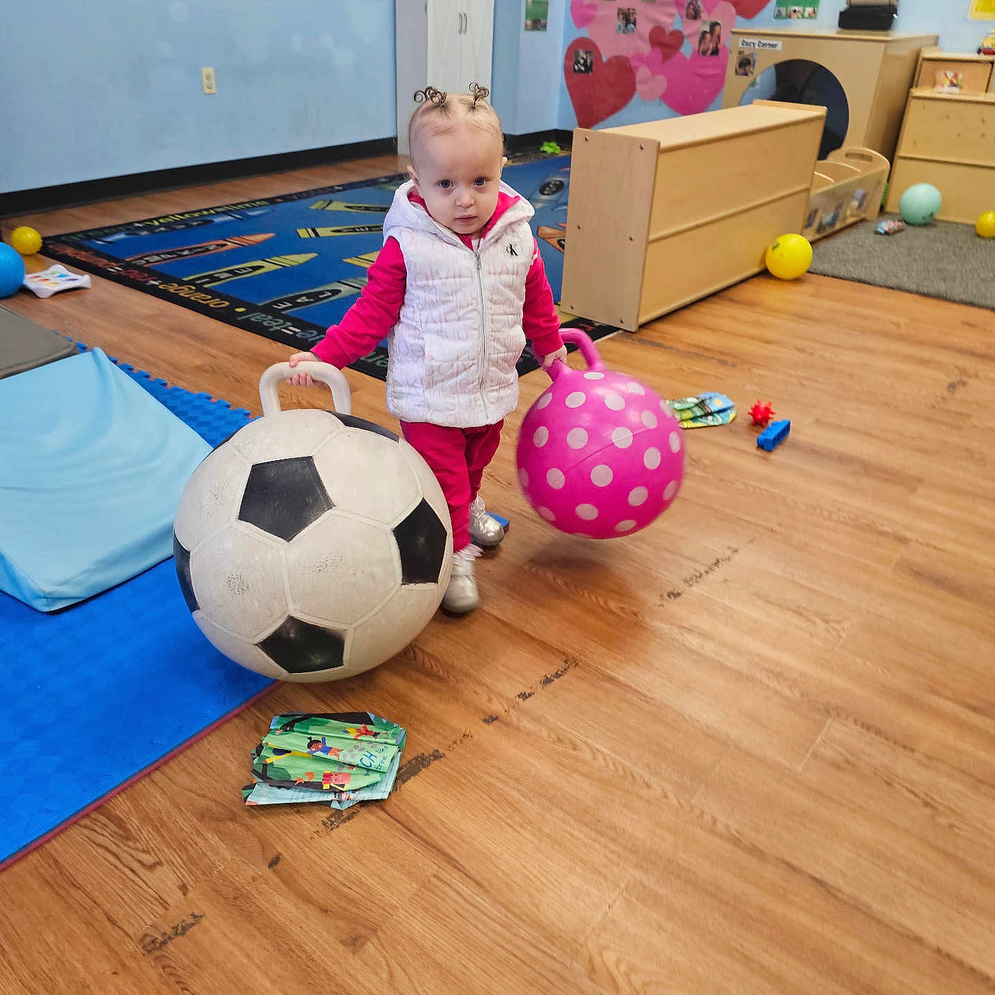 Monroe is registered to the contest to win money with this photo: ball, child, classroom, curly_hair, educational, floor, fun, hopper_ball, indoor, pink_clothing, play, playroom, rug, soccer_ball, toddler, toy, vest, wall_art, wood_floor, young_child