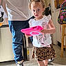 child, toddler, girl, portrait, indoors, standing, smiling, tablet, pink, sunglasses, leopard_print, skirt, white_shirt, curly_hair, fashion, backpack, adult, home, floor, photography