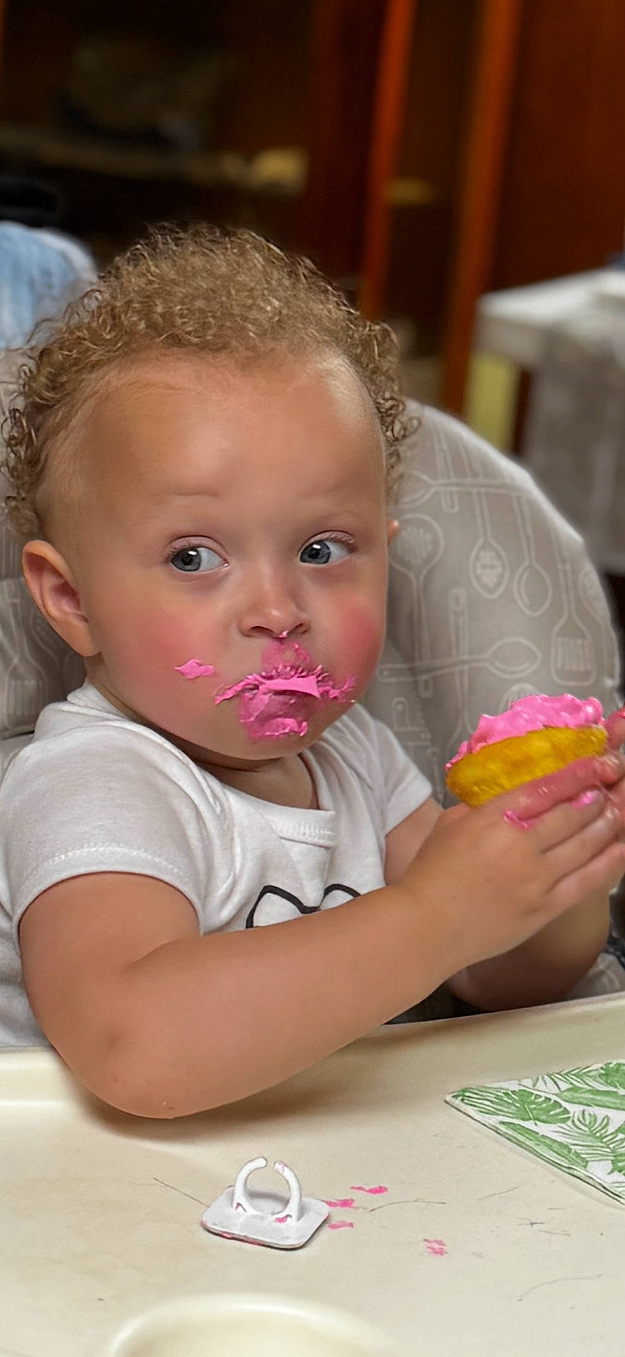 Monroe is registered to the contest to win money with this photo: baby, cheeks, child, clothing, cupcake, curly_hair, expression, face_paint, food, hands, high_chair, indoor, messy, person, pink_frosting, portrait, sitting, snack_time, table, toddler