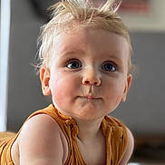 Raphaël a rejoint le concours — aidez-le/la à gagner de superbes lots ! baby, child, portrait, face, blue_eyes, blonde_hair, close_up, curious, tousled_hair, sleeveless_top, mustard_color, indoor, soft_light, chubby_arms, pout, expression, cute, infant, crawling, focus