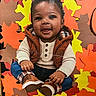baby, child, portrait, smiling, sitting, autumn, fall_leaves, paper_leaves, colorful, orange, yellow, brown, vest, sweater, boots, jeans, infant, indoor, close_up, playful