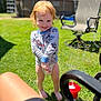 toddler, child, red_hair, barefoot, smiling, long_sleeve_shirt, diaper, bubbles, grass, outdoor, sunny, garden_chair, toy, playful, greenery, daylight, happy, person, lawn, summer
