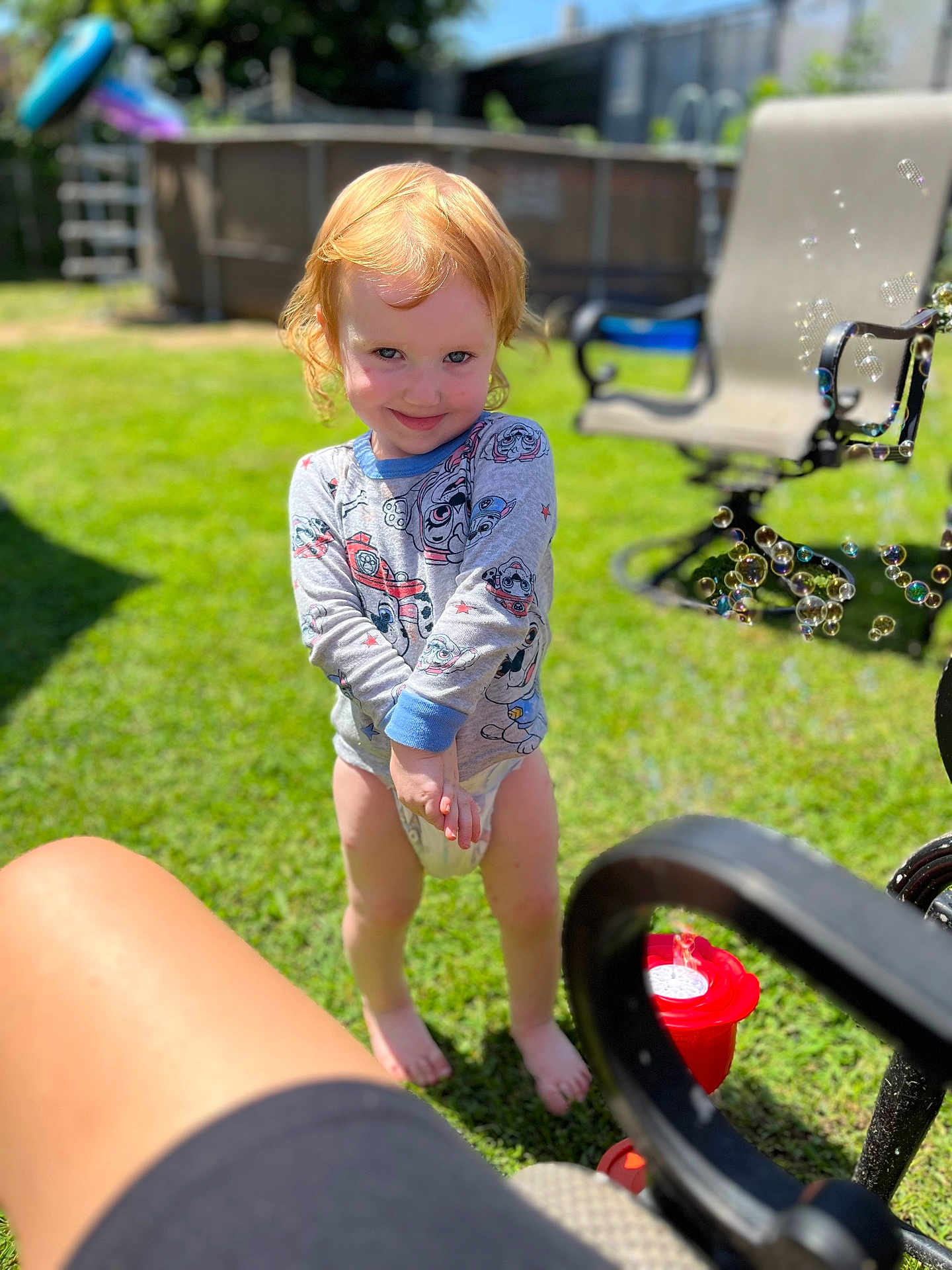 Ariela joined the competition — help win amazing prizes! toddler, child, red_hair, barefoot, smiling, long_sleeve_shirt, diaper, bubbles, grass, outdoor, sunny, garden_chair, toy, playful, greenery, daylight, happy, person, lawn, summer