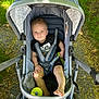 Summit is registered to the contest to win money with this photo: toddler, stroller, child, outdoor, sunlight, toy, grass, pavement, smile, clothing, foot, seatbelt, canopy, nature, baby, person, playful, summer, shade, happy