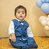 toddler, child, boy, blue_vest, bow_tie, white_shirt, sitting, indoor, balloons, decorations, curly_hair, curious_expression, woven_mat, portrait, cute, fashion, celebration, happy, floor, photography