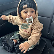 Shyne is registered to the contest to win money with this photo: baby, beanie, black_shoes, camo_pants, car_seat, casual, child, clothing, cute, face, footwear, headwear, hoodie, indoor, leather_seat, pacifier, portrait, sitting, toddler, young_child
