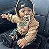baby, beanie, black_shoes, camo_pants, car_seat, casual, child, clothing, cute, face, footwear, headwear, hoodie, indoor, leather_seat, pacifier, portrait, sitting, toddler, young_child