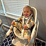 toddler, child, high_chair, pajamas, sunflower_pattern, smile, indoor, window_blinds, happy, socks, furniture, floor_mat, person, seat_belt, light, wooden_leg, wall, carpet, home, cute