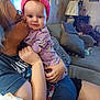 baby, child, adult, kiss, couch, living_room, headband, purple_clothing, pink, smile, affection, indoor, person, glasses, tattoo, arm, remote_control, pillow, lamp, wall_decor