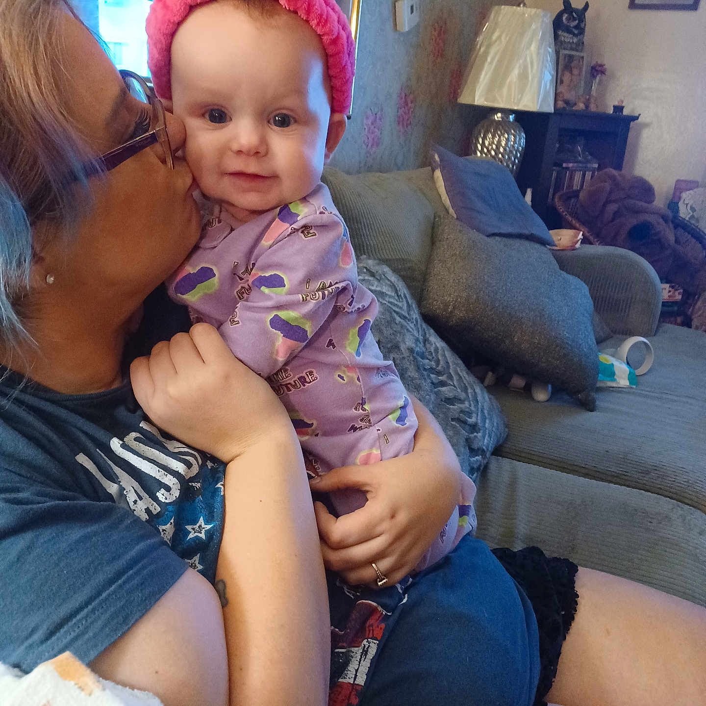 Harriett joined the competition — help win amazing prizes! adult, affection, arm, baby, child, couch, glasses, headband, indoor, kiss, lamp, living_room, person, pillow, pink, purple_clothing, remote_control, smile, tattoo, wall_decor